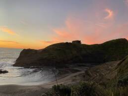 Sunset behind large outcrop on New Zealand coast